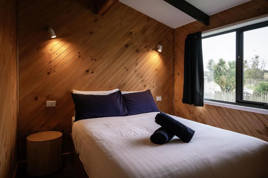 A wooden-paneled room with a bed, a small round table, and a window with a view.