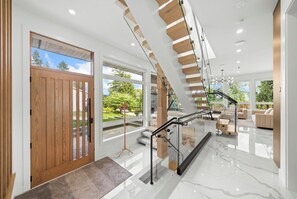 A modern interior with a wooden door, a staircase with glass railings, and a view of greenery outside. - North Shore Luxe Villa | Luxury 4BR Near Downtown Vancouver (North Vancouver)