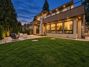 Uma casa moderna de dois andares com gramado bem cuidado e área de estar externa.