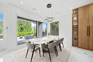 Uma sala de jantar moderna com uma mesa grande, cadeiras e vista para o verde lá fora.