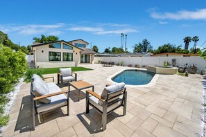 Un patio trasero con piscina, mobiliario de exterior y una casa moderna.