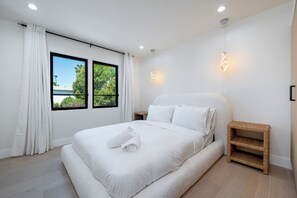 Un dormitorio con una cama grande, dos ventanas, una mesita de noche y una lámpara colgante.