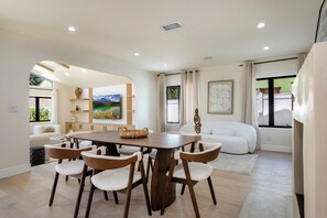 Un comedor moderno con una mesa y sillas de madera, un sofá y un cuadro de un paisaje montañoso.