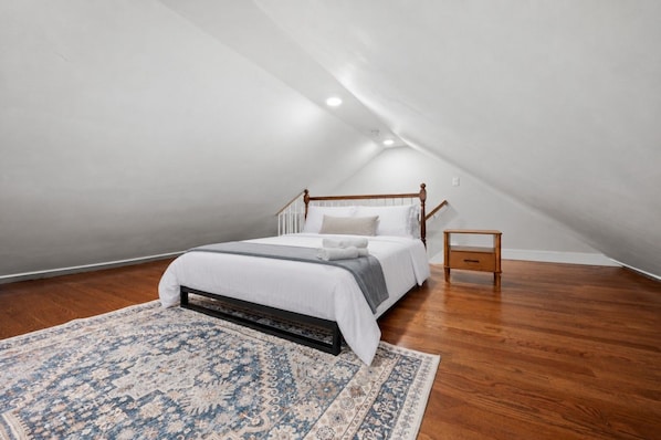 A bedroom with a sloped ceiling, a bed with a wooden frame, a nightstand, and a patterned rug.