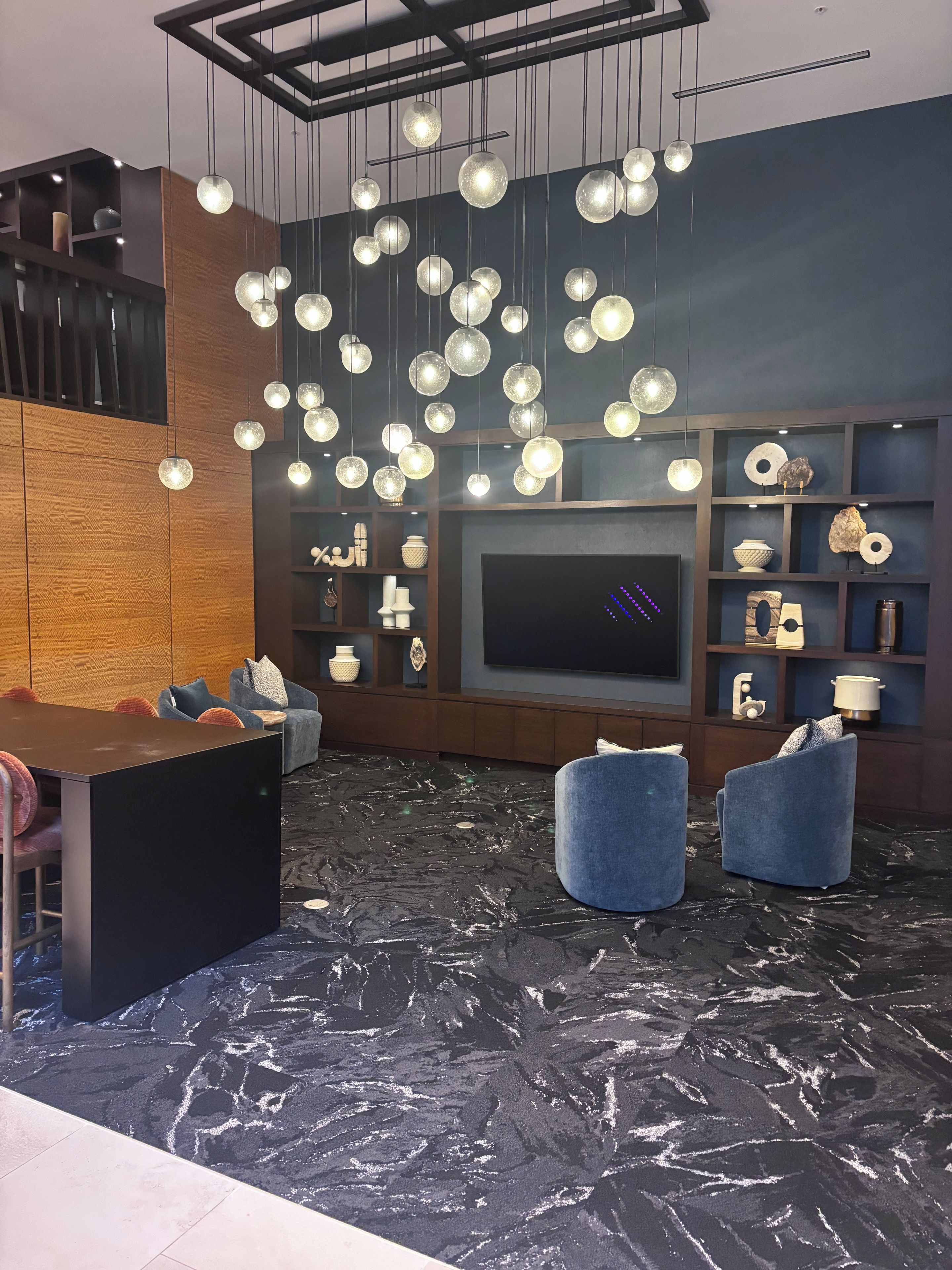 A modern living room with a black marble floor, a large flat-screen TV, and a variety of decorative items on shelves.