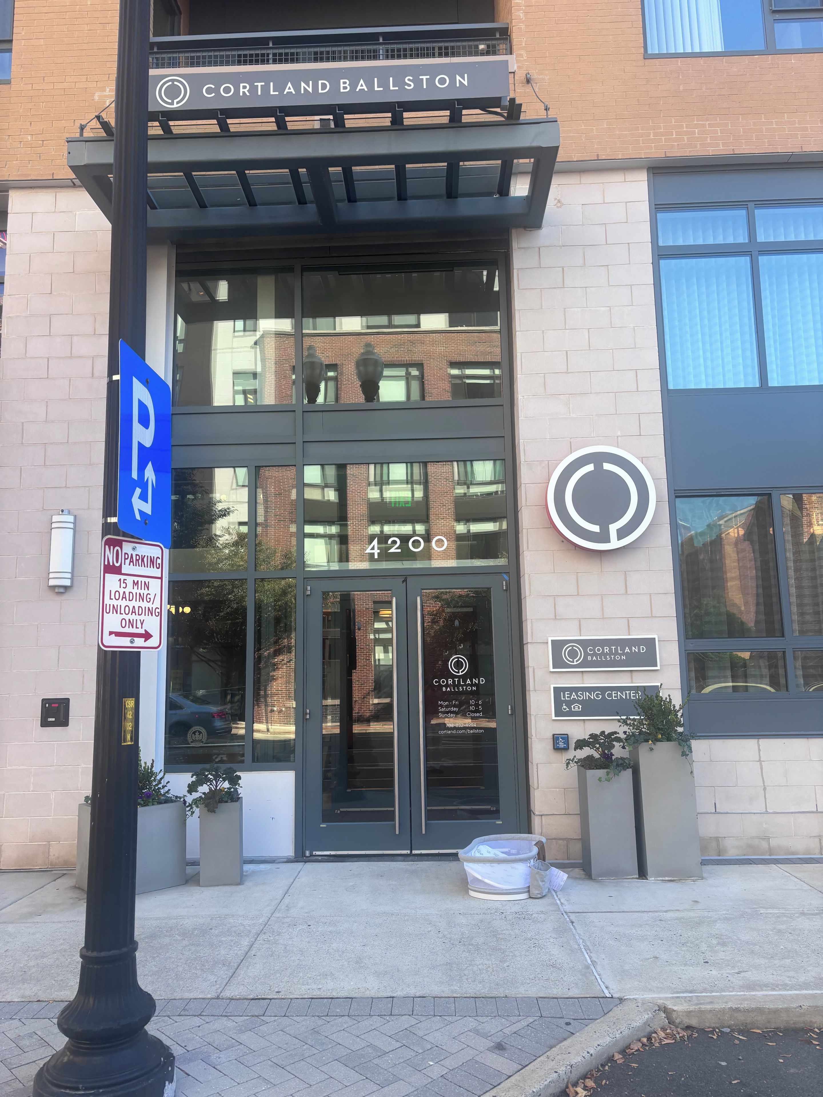 Een gebouwde ingang met een bord voor Cortland Ballston, een verhuurcentrum, en een parkeersbord waarop staat dat parkeren niet is toegestaan en alleen laden en lossen voor 15 minuten.