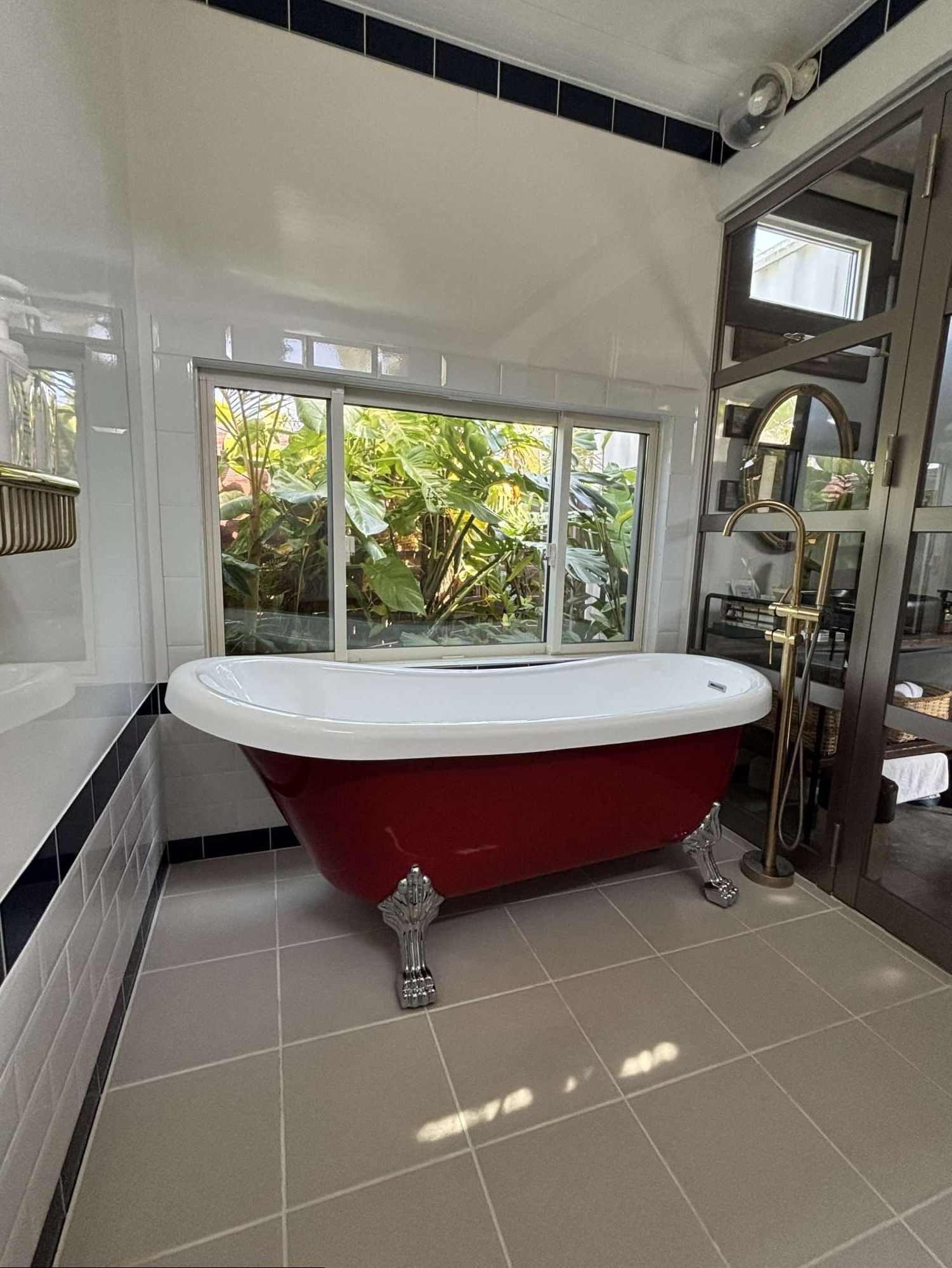 Une salle de bain avec une baignoire sur pieds, une fenêtre donnant sur un espace verdoyant et un sol carrelé.