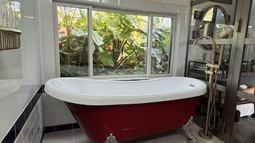 A bathroom with a freestanding bathtub, a window with a view of greenery, and a tiled floor.