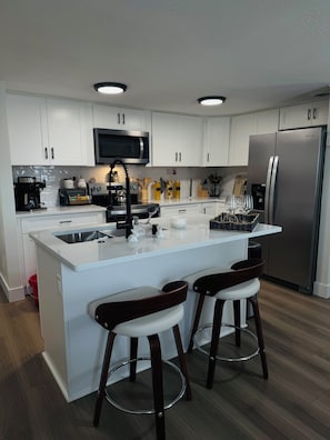 Een moderne keuken met witte kastjes, roestvrijstalen apparatuur en een centraal eiland met barkrukken.