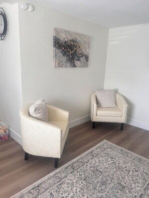 Ein Zimmer mit zwei Sesseln, einem gemusterten Teppich und einem an der Wand hängenden abstrakten Gemälde.