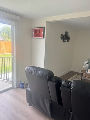 Ein Wohnzimmer mit einer Schiebetür zu einem Garten, einem schwarzen Ledersofa, einem kleinen Tisch mit einer Vase und einer Wanddekoration.
