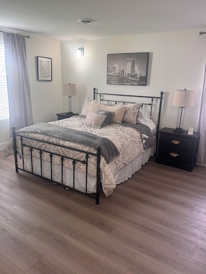 Een slaapkamer met een bed, nachtkastjes, een lamp, een foto aan de muur en een raam met gordijnen.