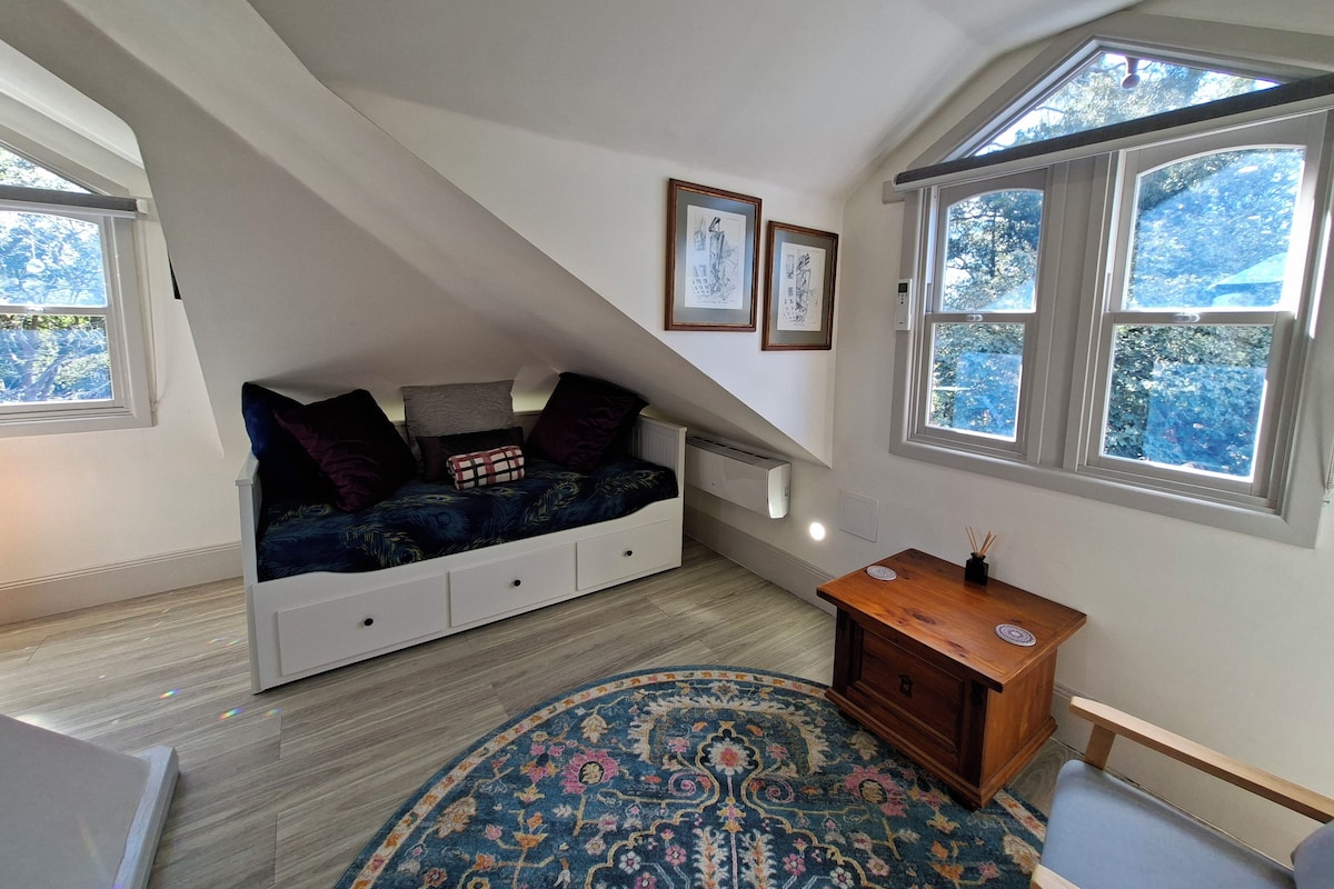 Une pièce avec un plafond en pente, un lit encastré doté de tiroirs de rangement, une petite table d’appoint en bois, un tapis à motifs et des œuvres d’art encadrées accrochées aux murs.