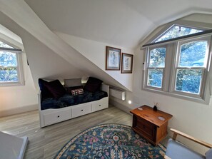 Une pièce avec un plafond en pente, un lit encastré doté de tiroirs de rangement, une petite table d’appoint en bois, un tapis à motifs et des œuvres d’art encadrées accrochées aux murs.