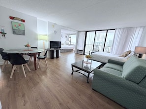 Une chambre d’hôtel moderne dotée d’un coin repas, d’un canapé, d’une télévision et d’un balcon offrant une vue sur la ville.