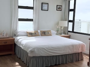 Une chambre avec un grand lit, deux oreillers ornés du mot «Relax», une table de chevet avec une lampe, et une vue sur la ville par la fenêtre.