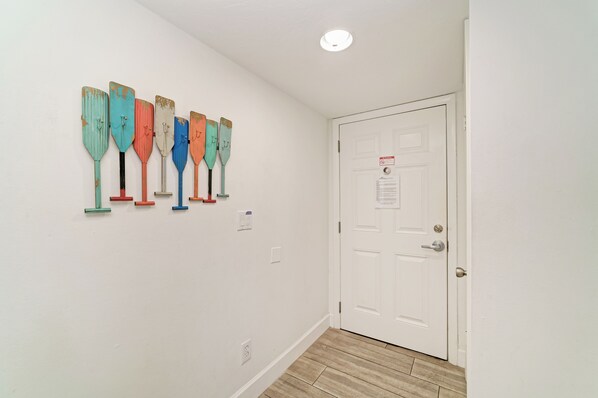 A hallway with a white door, a wall-mounted light fixture, and a row of colorful paddles. - Your Family-Friendly Beach Getaway on Longboat Key (Longboat Key)