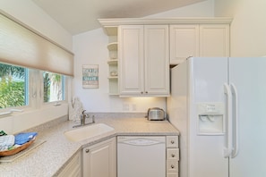A kitchen with white cabinets, a granite countertop, a built-in dishwasher, and a refrigerator. - Your Family-Friendly Beach Getaway on Longboat Key (Longboat Key)