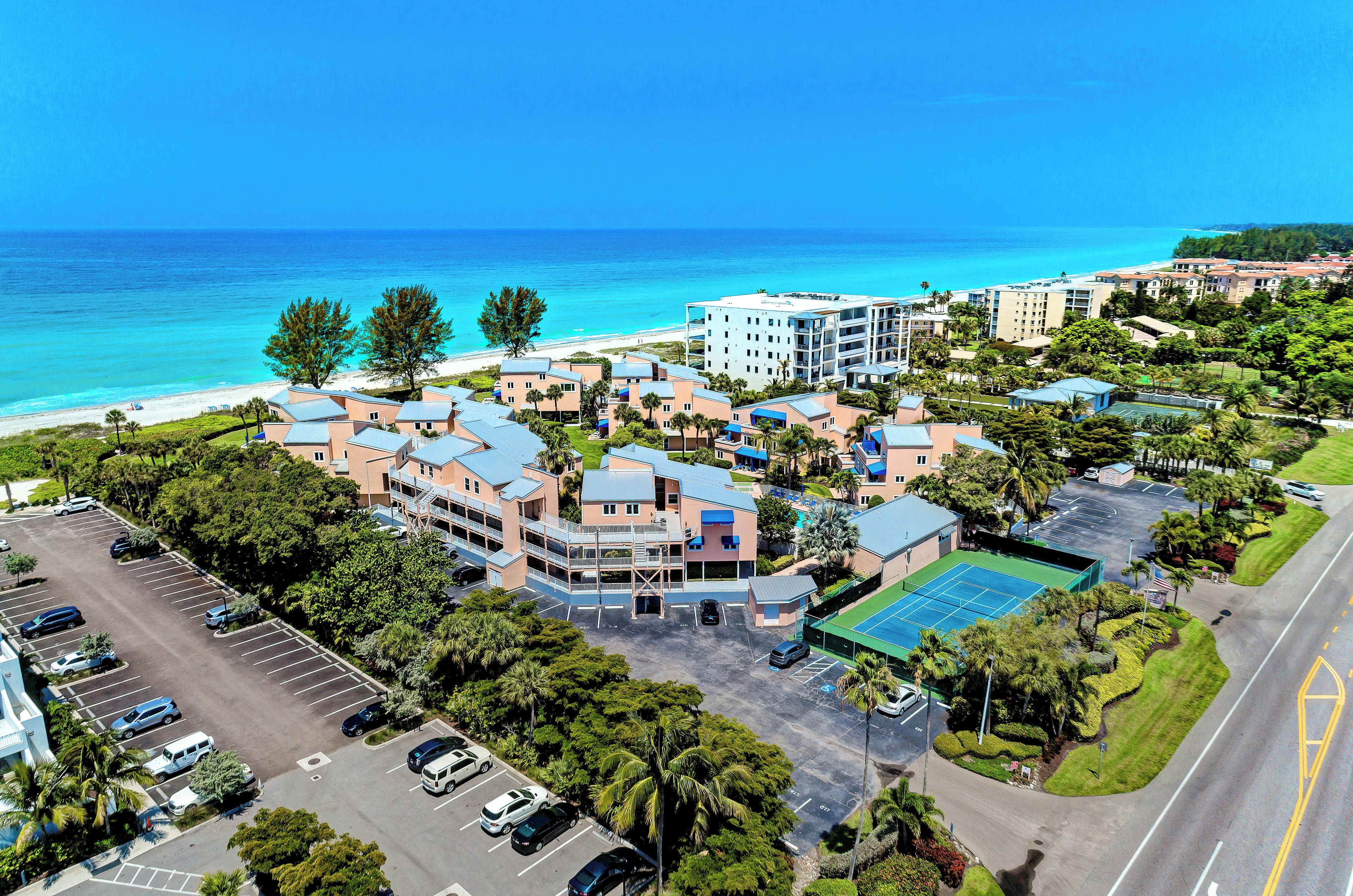A coastal hotel with multiple buildings, a parking lot, and a tennis court.