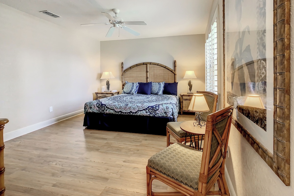 A bedroom with a bed, a chair, a table, a ceiling fan, and a wall with a patterned design.