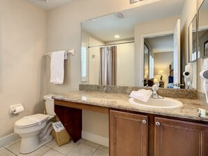 A bathroom with a toilet, sink, mirror, and shower area. - Anna's Regal Townhome - Comfort & Style (Davenport)
