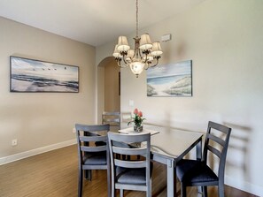 A dining area with a chandelier, four chairs, a table, and two wall-mounted paintings. - Anna's Regal Townhome - Comfort & Style (Davenport)