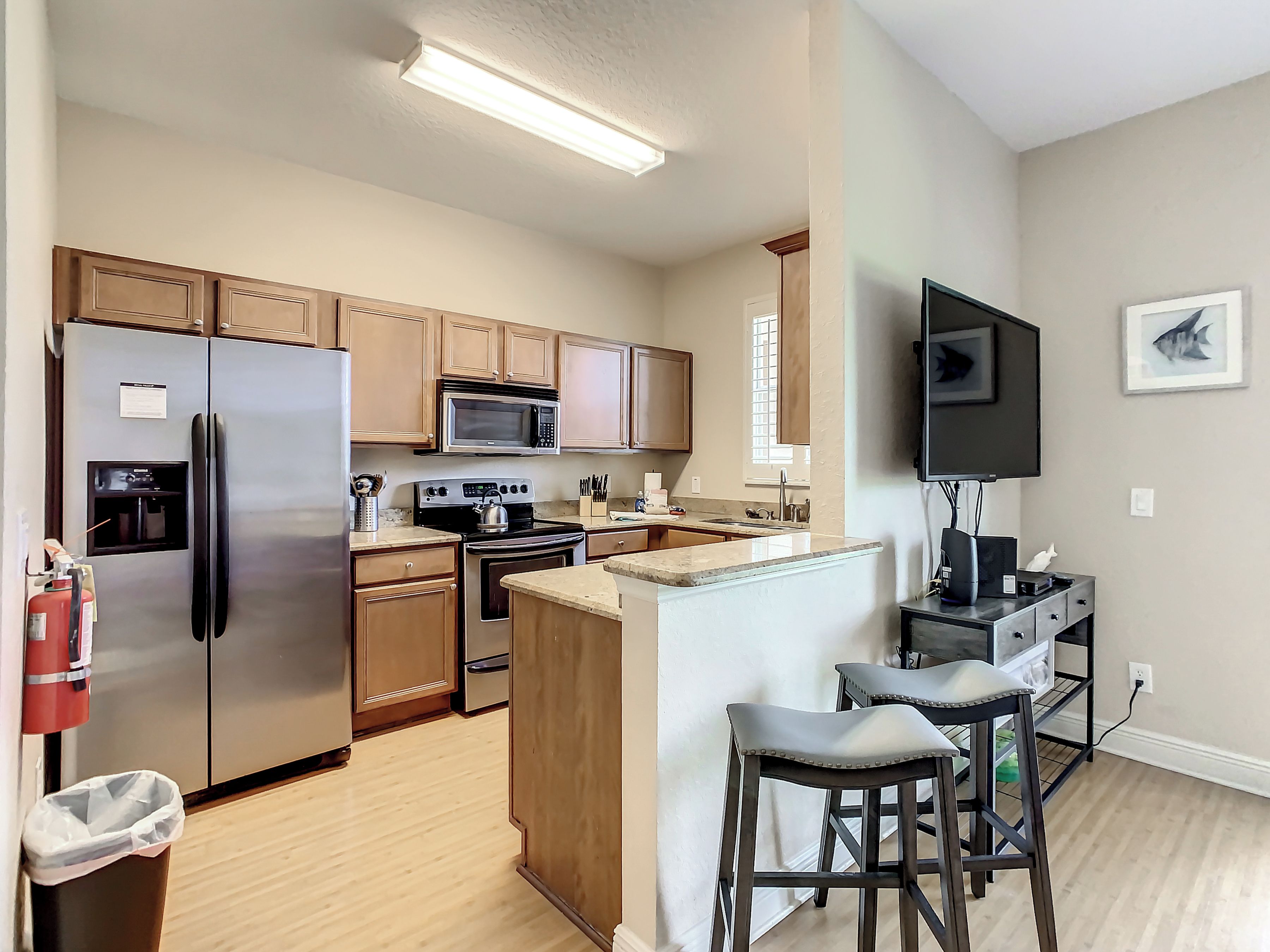 A modern kitchen with stainless steel appliances, wooden cabinets, and a bar area with stools.