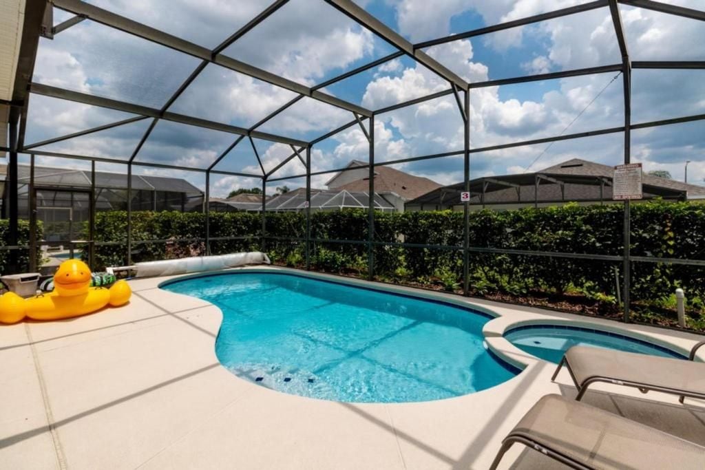 A swimming pool with a glass enclosure, surrounded by a hedge and a clear sky.