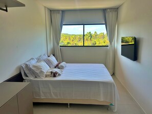 Habitación de hotel con una cama, un televisor montado en la pared y una ventana con vistas a la vegetación.