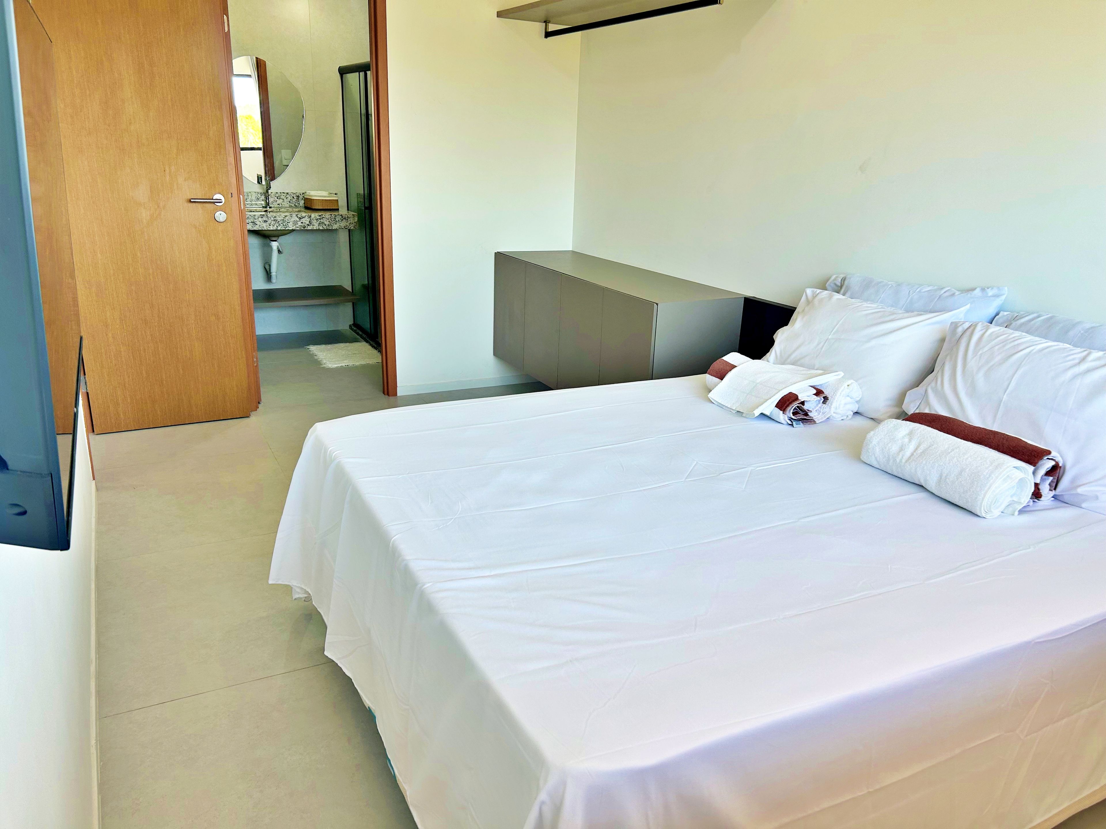 A hotel room with a bed, a wooden door, a bathroom with a mirror, and a white wall.