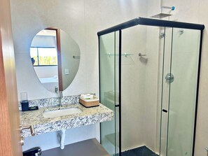 Un baño moderno con encimera de granito, un espejo redondo, cabina de ducha con paredes de vidrio y un perchero para toallas.