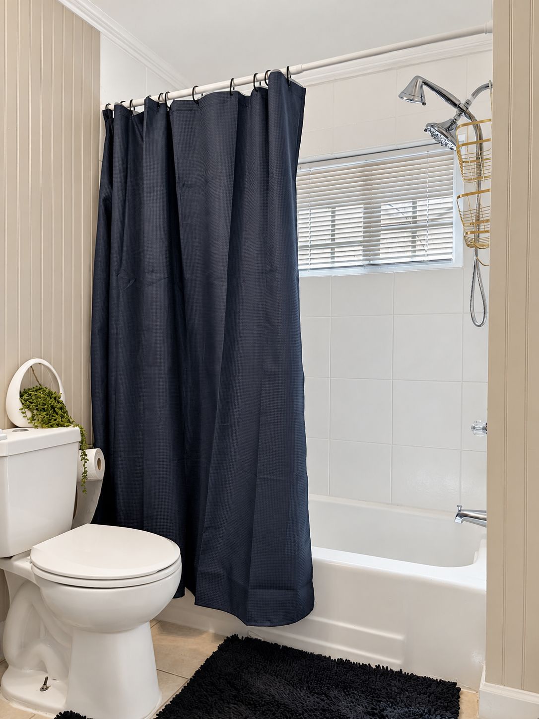 Une salle de bain avec des toilettes blanches, un rideau de douche bleu foncé, une baignoire blanche et un tapis noir.