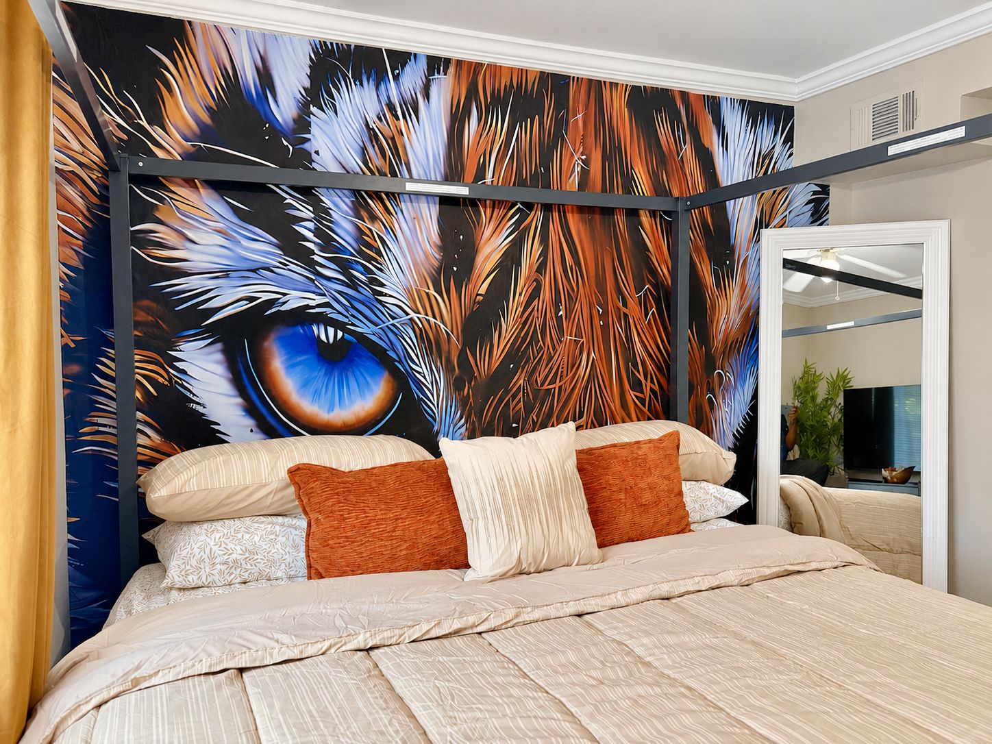 Une chambre à coucher avec un grand lit, une tête de lit agrémentée d’un miroir et une fresque murale représentant un œil.