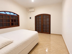 Een slaapkamer met een bed, een raam, een airconditioning en een deur met ruitpanelen.