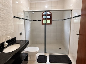 Een moderne badkamer met een douchecabine van glas, een wit toilet en een zwart aanrechtbakje.