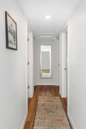 A narrow hallway with wooden flooring, white walls, and a door at the end. - 4BR Austin Home Near Walter E. Long Park (Austin)