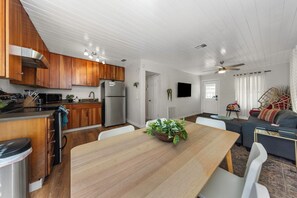 Une cuisine moderne avec des meubles en bois, un réfrigérateur en acier inoxydable et un coin repas comprenant une table et des chaises en bois.