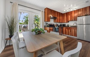 Une cuisine moderne avec des meubles en bois, un réfrigérateur en acier inoxydable et un coin repas comprenant une table en bois et des chaises blanches.