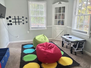 Ein Zimmer mit Teppichboden, einem Bücherregal, einem Schreibtisch mit Stuhl und Sitzsäcken.