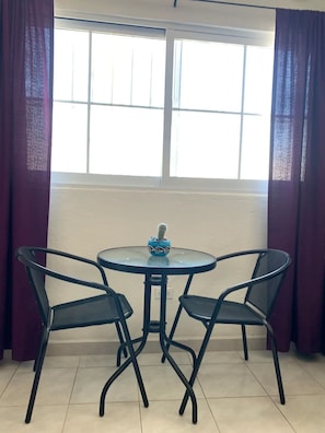 Een kleine ronde tafel met twee stoelen, een cactus in een decoratieve pot en een raam met gordijnen.
