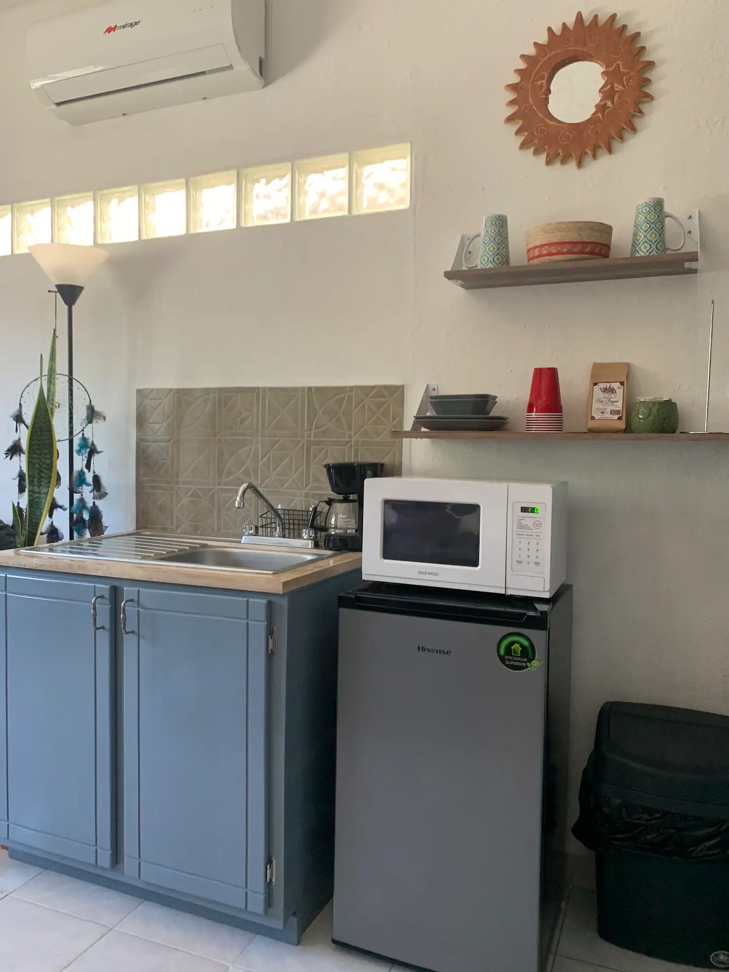 A compact kitchen with a sink, a microwave, a refrigerator, and a decorative wall shelf.