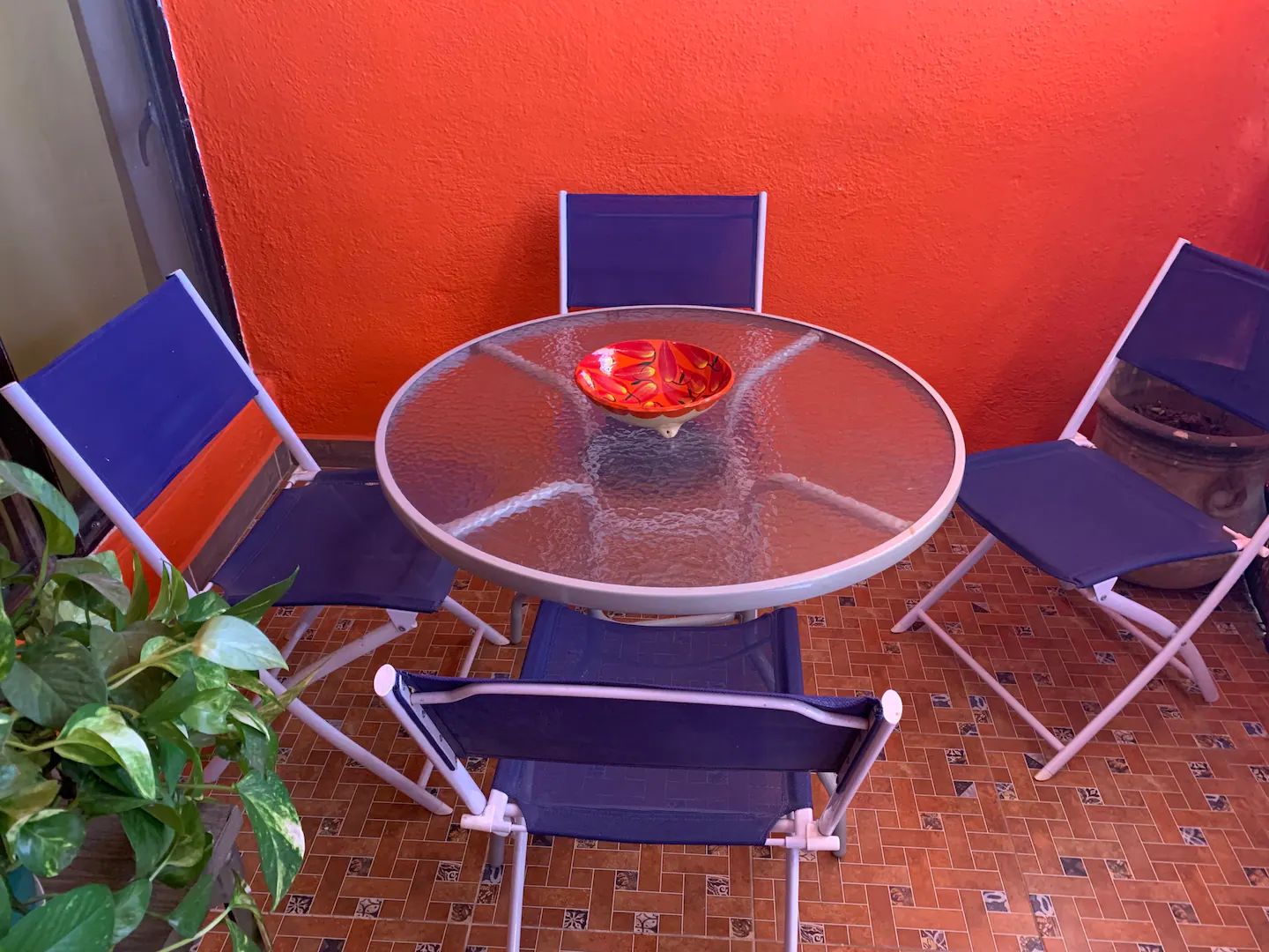 A round glass table with a red bowl in the center, surrounded by four blue chairs.
