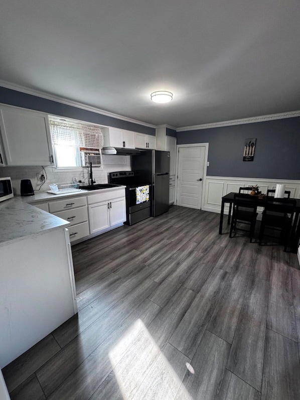A modern kitchen with white cabinets, a black refrigerator, and a dining area with a table and chairs.