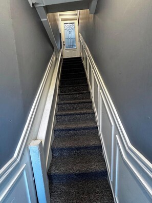 Eine enge Treppe mit Teppichboden führt zu einer Tür, deren Fenster ein dekoratives Glasdesign aufweist.