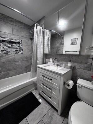 Une salle de bain moderne équipée d’une baignoire, d’un lavabo, de toilettes et d’un rideau de douche.