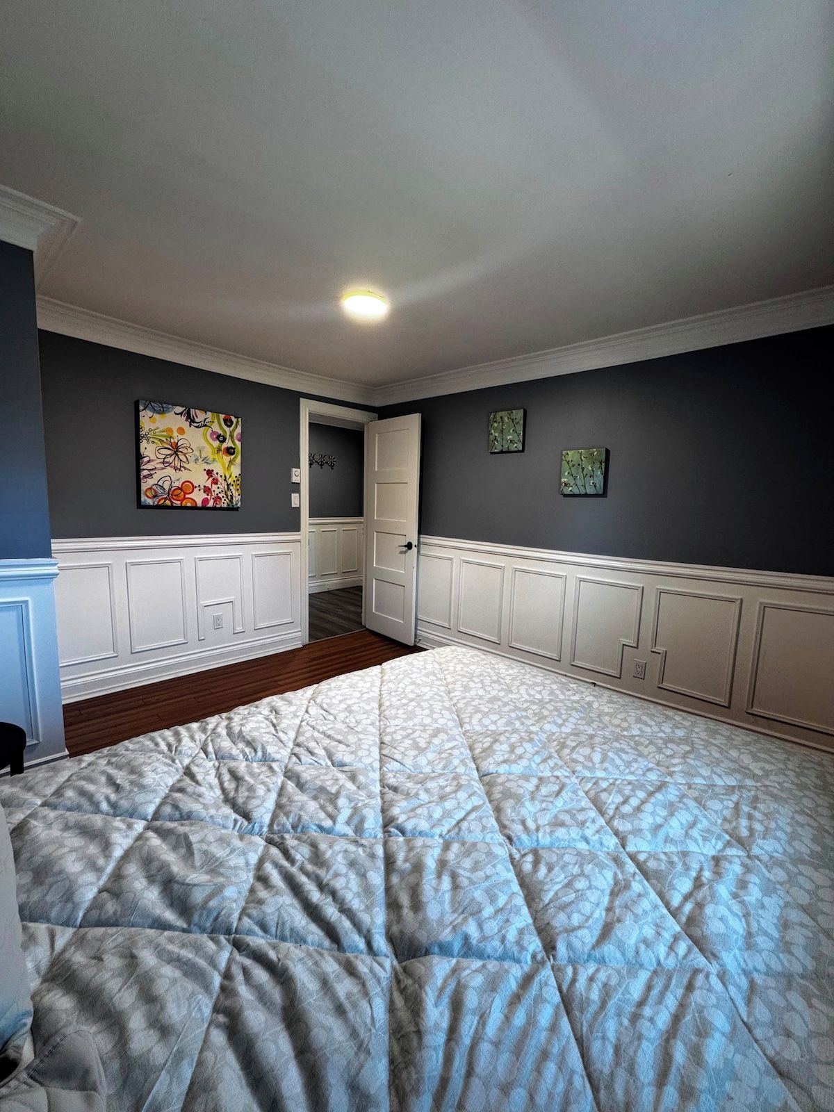 Une chambre avec un grand lit, une porte donnant sur une autre pièce et deux œuvres d’art accrochées au mur.