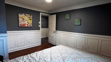 Une chambre avec un grand lit, une porte donnant sur une autre pièce et deux œuvres d’art accrochées au mur.