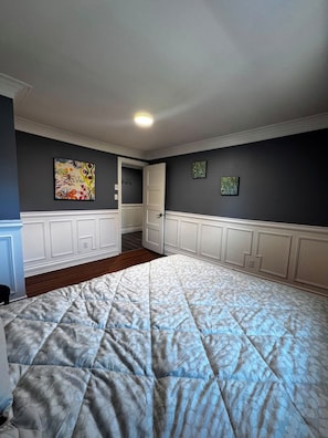 A bedroom with a large bed, a door leading to another room, and two wall-mounted artworks.