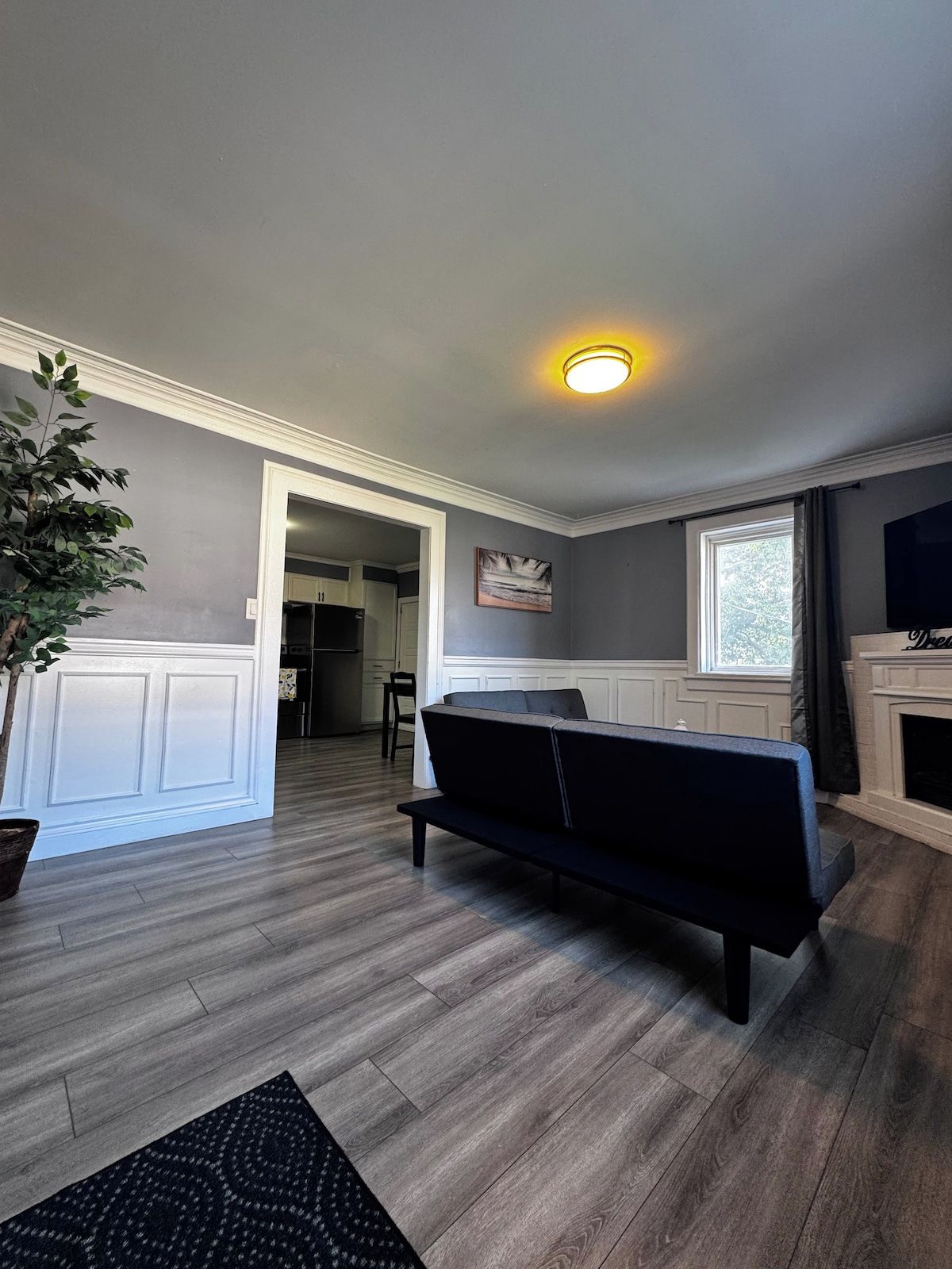 Una sala de estar moderna con un sofá oscuro, piso de madera, chimenea y un ventanal grande.