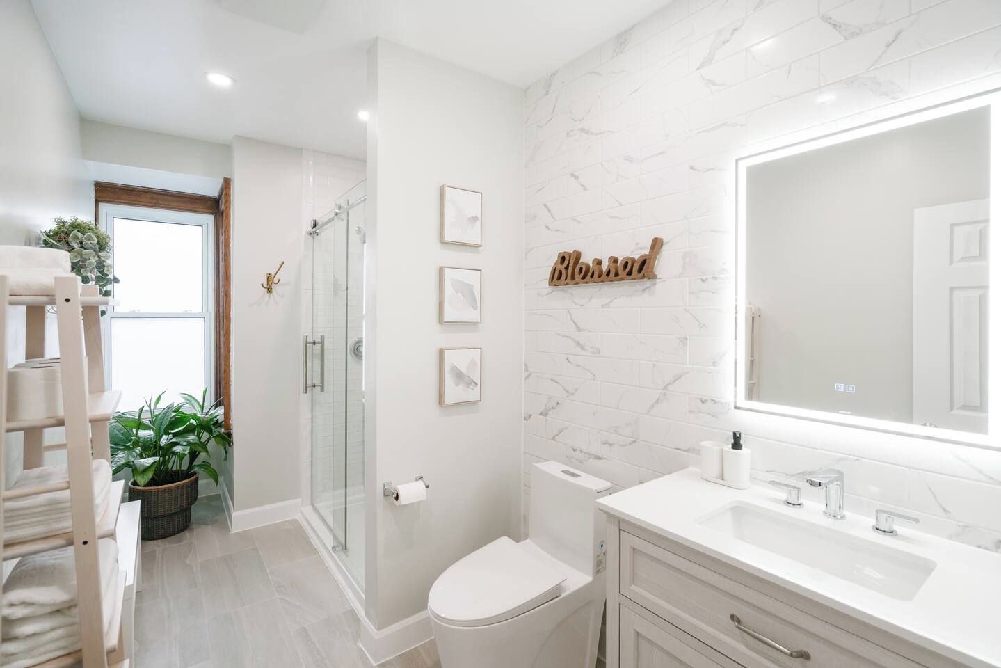 A modern bathroom with a glass shower enclosure, a toilet, a sink with a large mirror, and framed artwork on the wall.